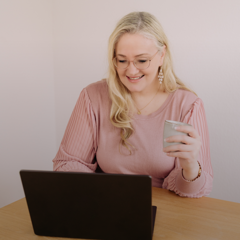 Lilli Heinze Seminare und Kurse Lächelnde Frau sitzt an einem Tisch, hält ein Mikrofon und arbeitet am Laptop.